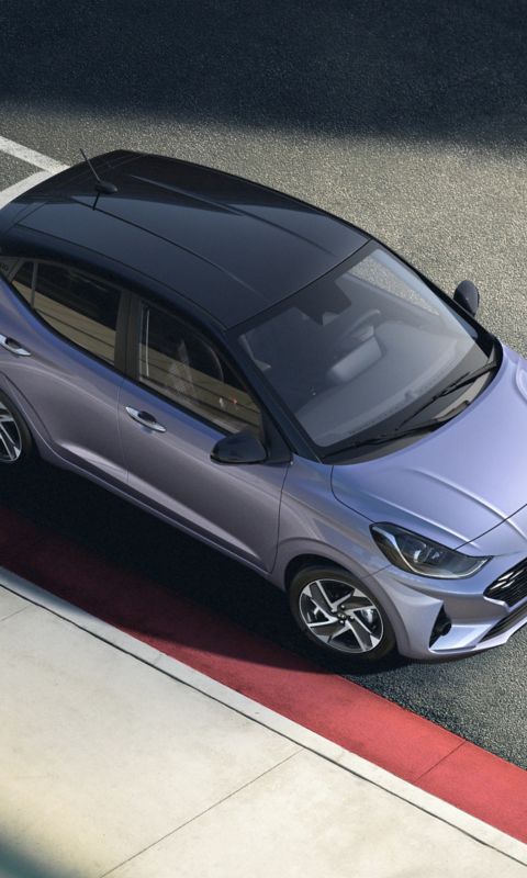 Hyundai i30 seen from rear three-quarter driving on a city street in front of modern buildings.