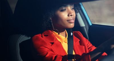 A woman sitting behind the wheel of her Hyundai KONA, looking very relaxed.