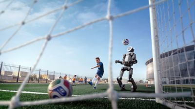 Zwei Kinder spielen Fußball auf einer ruhigen Straße, während ein modernes Hyundai-Auto und ein humanoider Roboter am Straßenrand stehen; Szene aus einer Kampagne zur Kooperation mit der FIFA 2026.