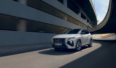 The Hyundai TUCSON Hybrid driving over a bridge in the city with the skyline in the background.