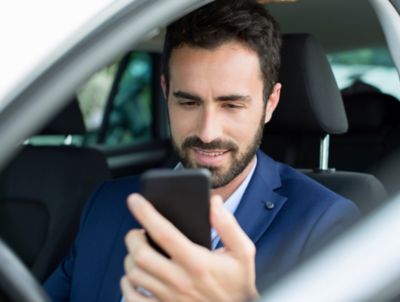 Een klant zit in de auto en houdt zijn mobiele telefoon vast om een afspraak online in te plannen.