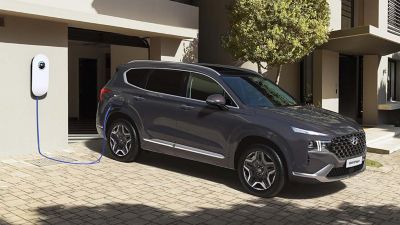 The Hyundai SANTA FE Plug-in Hybrid parked in a street, two couples standing around the charging station.