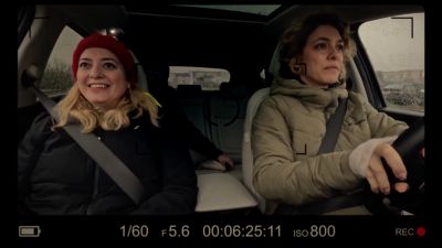 The woman, smiling, drives with the steering wheel on the right side of the car, enjoying the journey