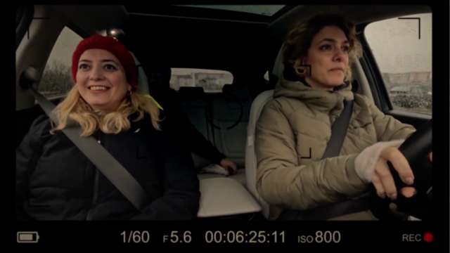The woman, smiling, drives with the steering wheel on the right side of the car, enjoying the journey