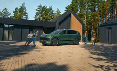 Vista laterale del SUV elettrico a 7 posti Hyundai IONIQ 9 con bambini che corrono intorno davanti a una casa. 