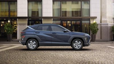 The all-new Hyundai KONA show from the side parked in front of modern building.