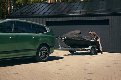 Una Hyundai IONIQ 9 è parcheggiata davanti a un garage. Al gancio di traino del veicolo è fissato un rimorchio coperto per barche. Gancio di traino retrattile sul retro del SUV elettrico Hyundai IONIQ 9.