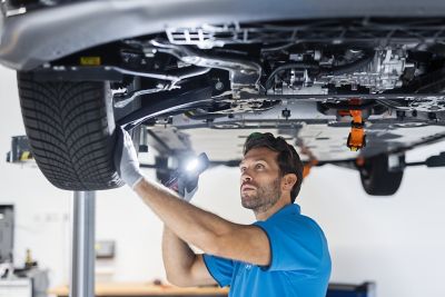 Otomobil servis istasyonu arka planı. Teknisyen, asansörle kaldırılmış otomobil üzerinde onarım ve bakım işlemi yapıyor.