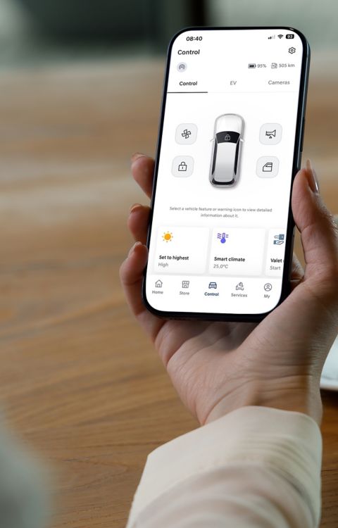 Hand holding a smartphone displaying an electric vehicle control app with remote climate settings and vehicle status.