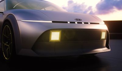 Close-up of the Hyundai Concept THREE front, highlighting slim LED headlights, illuminated square grille lights, and aerodynamic curves at sunset.