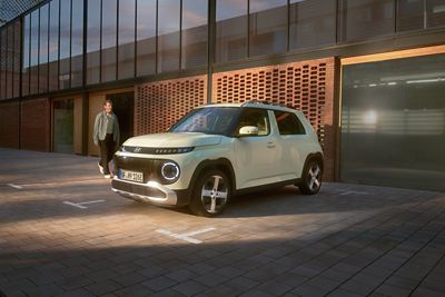 Un Hyundai INSTER si trova in un cortile, mentre una persona si avvicina da un portone sotto la luce soffusa della sera.