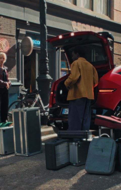 Red Hyundai IONIQ 3 parked side view on a city street, with luggage beside the car.