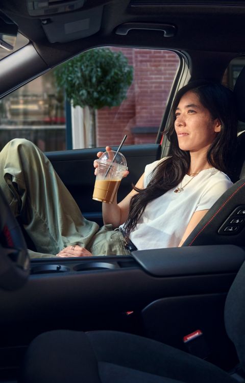 Interior view of a Hyundai IONIQ 3 showing a person seated in the front passenger seat, with the centre console and cup holders