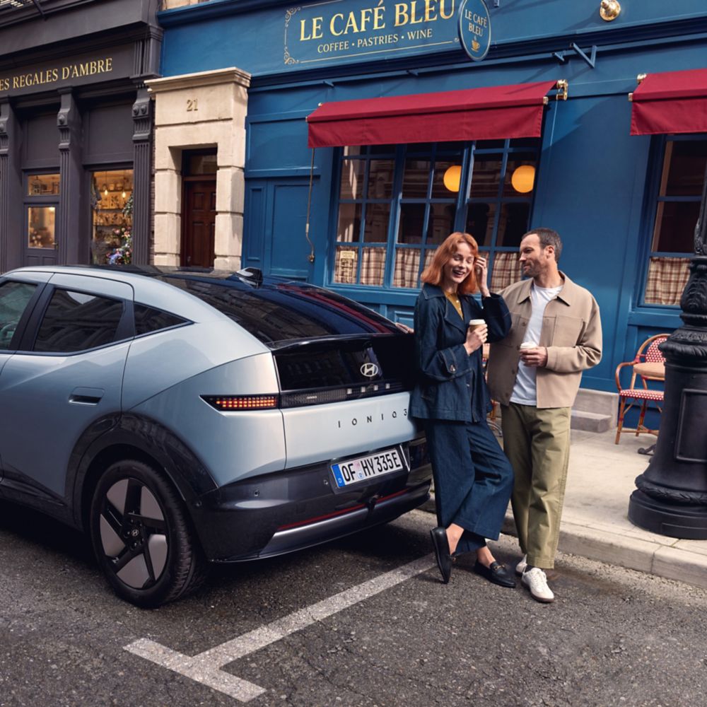 Hyundai IONIQ 3 parkerad utanför ett kafé med två personer intill bilen.