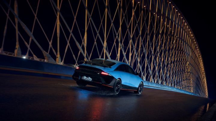 Una Hyundai IONIQ 6 N attraversa un ponte di notte, circondata da elementi architettonici illuminati.