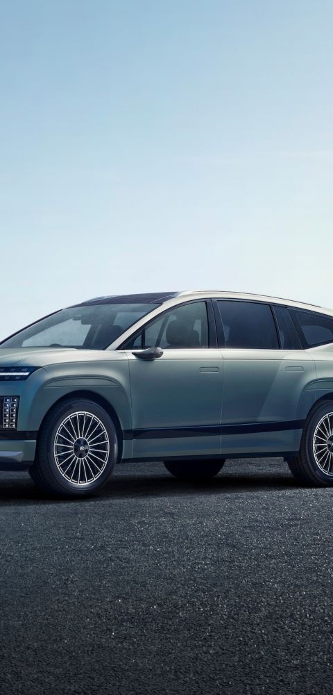 A Hyundai IONIQ 9 is parked on a paved surface under a clear sky, showcasing sleek design features like narrow headlights and large wheels.