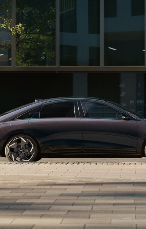 Hyundai IONIQ 6 electric sedan shown from street level parked with modern building in background.