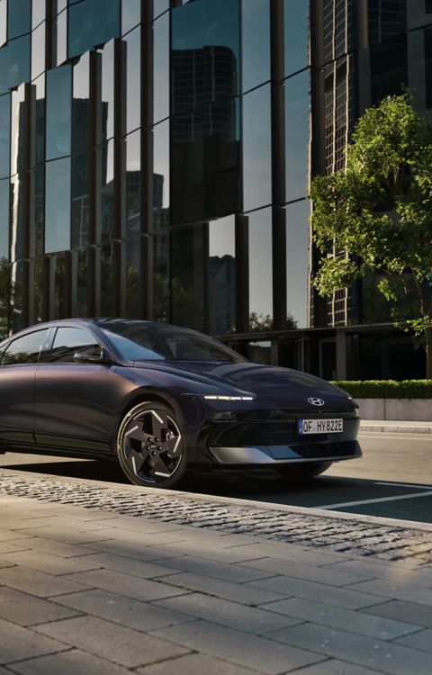 Hyundai IONIQ 6 electric sedan shown from the side parked on a city street with high rise buildings.