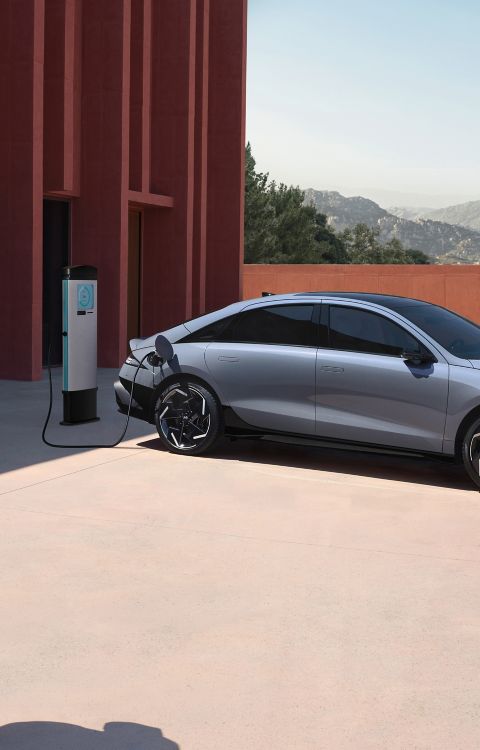 A man walking away from the Hyundai IONIQ 6 with a coffee cup while the car is plugged in to charge.