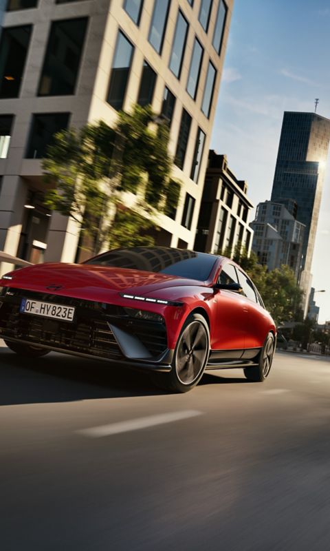  A red Hyundai IONIQ 6 N Line driving through a modern cityscape.