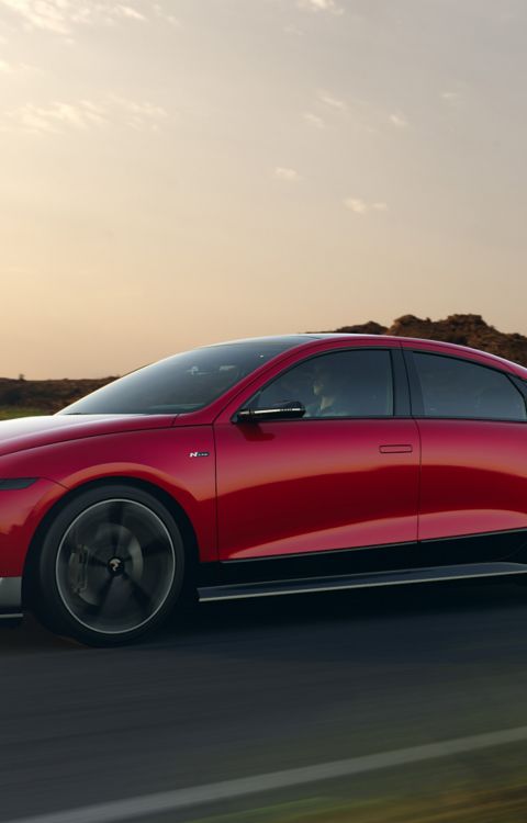 The new Hyundai IONIQ 6 N Line in red driving down a highway with hills in the background. 