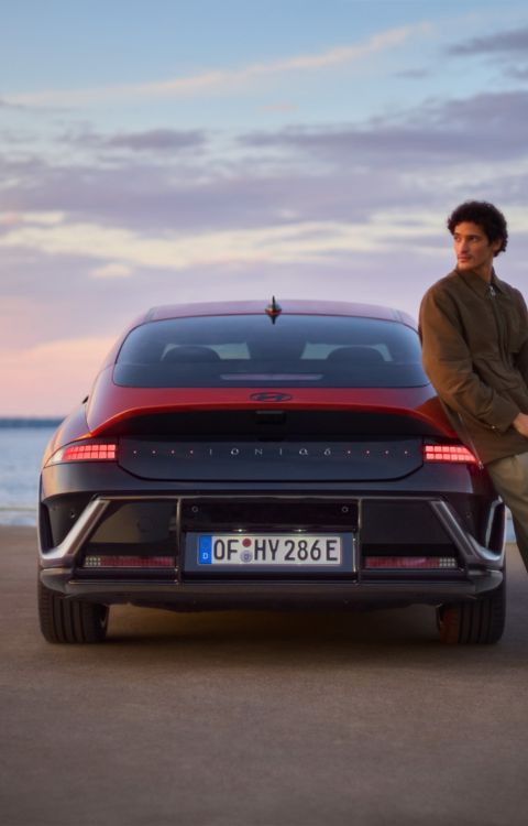 A man leaning on the side of a Hyundai IONIQ 6 N Line parked next to the ocean.
