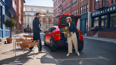 Deux personnes déchargent un meuble du coffre de IONIQ 3 rouge dans une rue en ville.