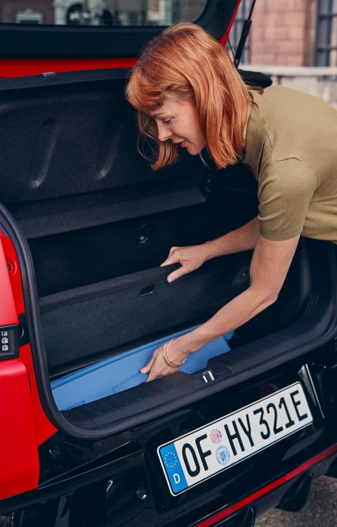 Une femme range des affaires dans le compartiment de rangement sous le plancher du coffre Megabox de la Hyundai IONIQ 3.