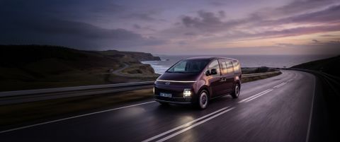 Hyundai STARIA ELECTRIC driving along a coastal road at sunset.