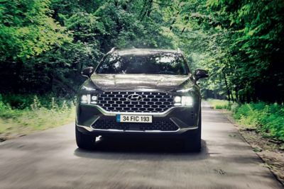 Hyundai KONA Elektrik SUV’un gün ışığı altında görüntüsü ve yolcu kapısına doğru yürüyen bir bir adam. 
