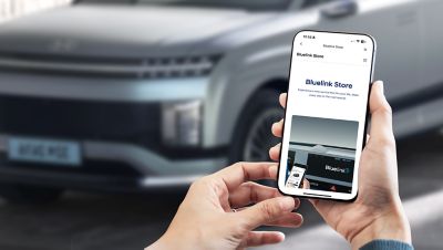 Person holding a smartphone with the Bluelink Store app open in front of a modern car.
