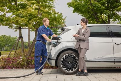 Technician charging an electric car while a person in a gray suit stands nearby with a phone.