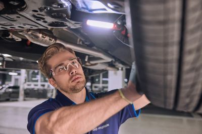 Hyundai mechanic inspecting the underside of a vehicle near the tire.